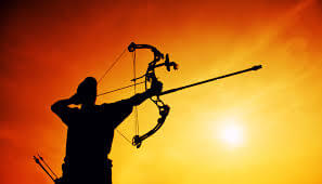 An archer taking aim while the sun is setting in the background
