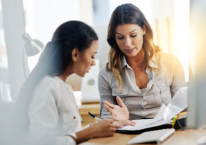 Shot of two young businesswomen talking to each other while being seated in the office at work