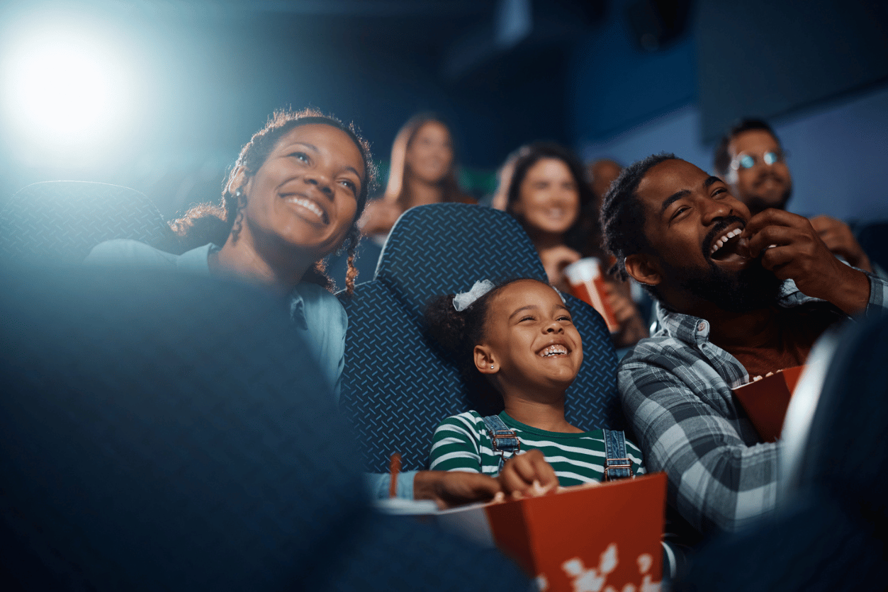 Vue International + InMoment: image of a family consisting of a mother, child and father smiling while watching a moving in a movie theater and eating popcorn