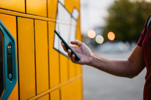 Handsome mid-adult man picking up his package from an electronic parcel locker using his smart phone.